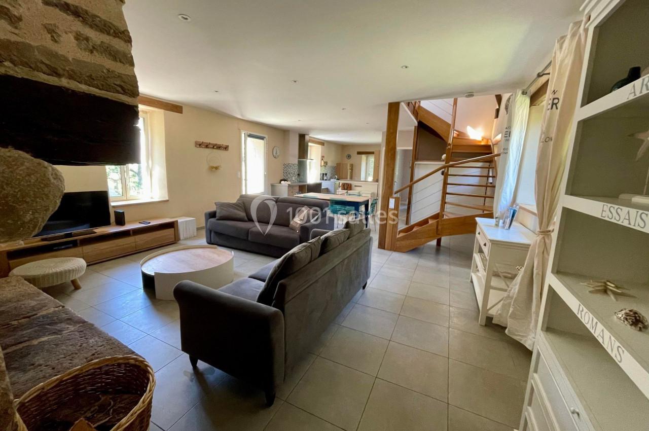 Salon lumineux avec canapé gris, table basse en bois, escalier en bois et étagères blanches dans un espace ouvert.