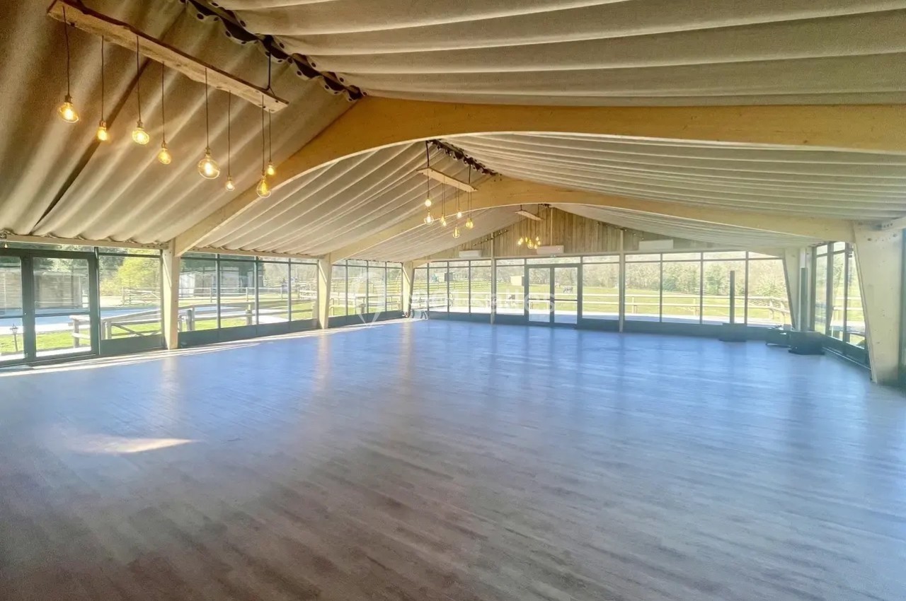 Salle spacieuse avec parquet clair, grandes baies vitrées et plafond en toile tendue, éclairée par des suspensions…