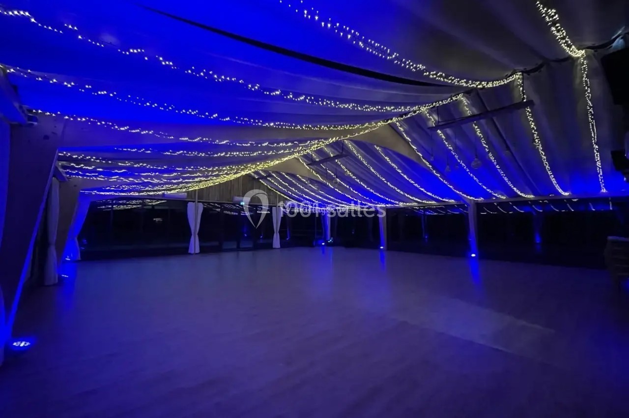 Plafond décoré de guirlandes lumineuses bleues et blanches dans un grand espace intérieur sombre.