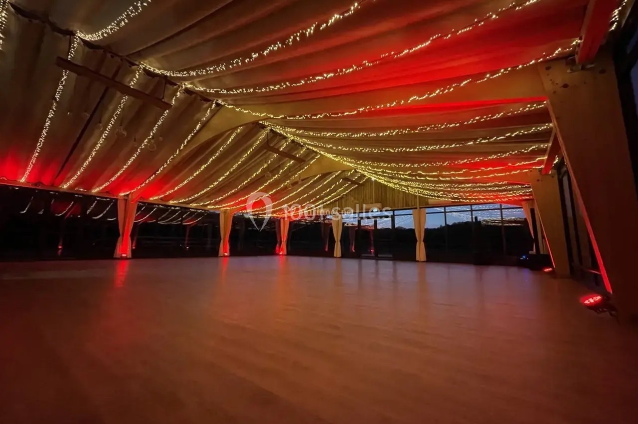 Plafond décoré de guirlandes lumineuses rouges et dorées dans une grande salle vide avec un sol en bois.