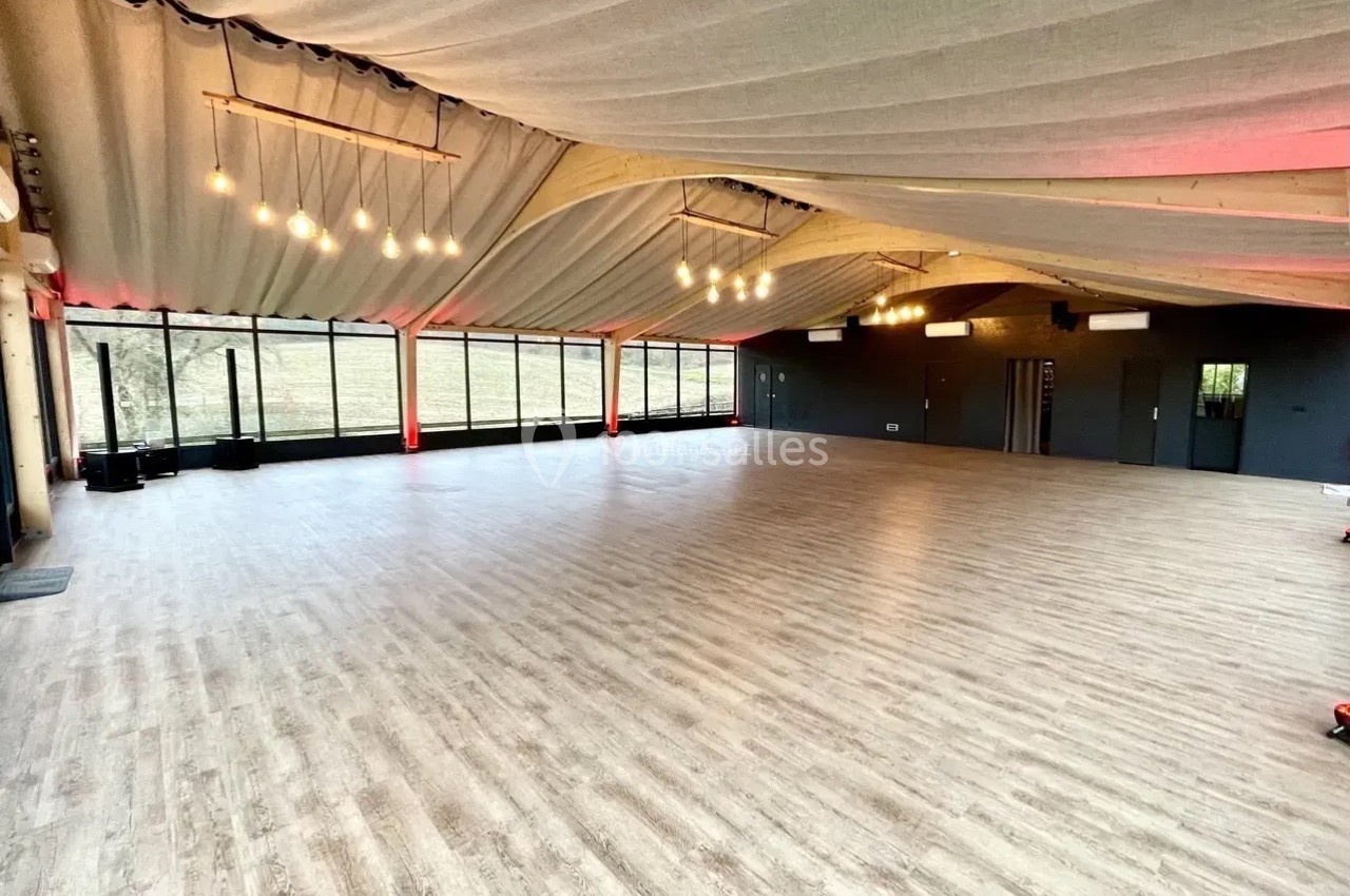 Salle spacieuse avec parquet clair, plafond en tissu tendu et grandes baies vitrées laissant entrer la lumière naturelle.