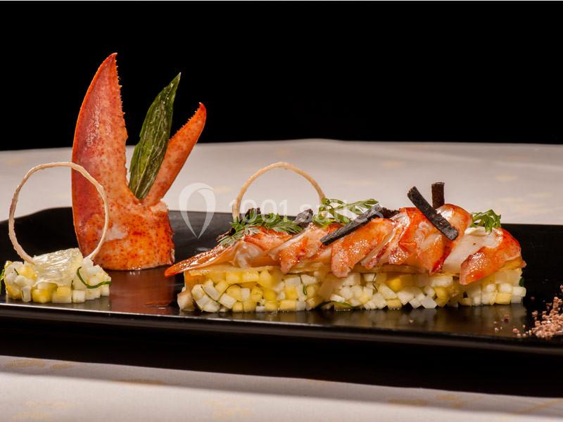 Plat gastronomique composé de morceaux de homard, légumes finement coupés et décorations élégantes sur une assiette noire.