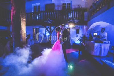Un couple en tenue de mariage se tient sur un balcon en pierre devant une fenêtre illuminée.
