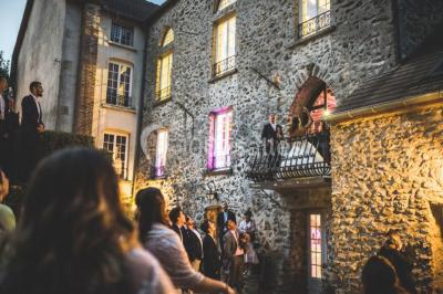 Un couple en tenue de mariage se tient sur un balcon en pierre devant une fenêtre illuminée.