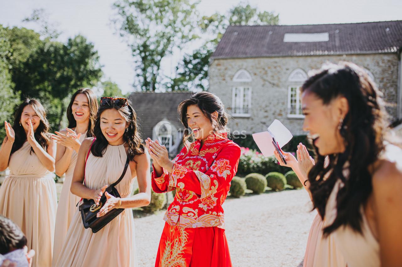 Un groupe de femmes souriantes applaudissent à l'extérieur devant un bâtiment en pierre par une journée ensoleillée.