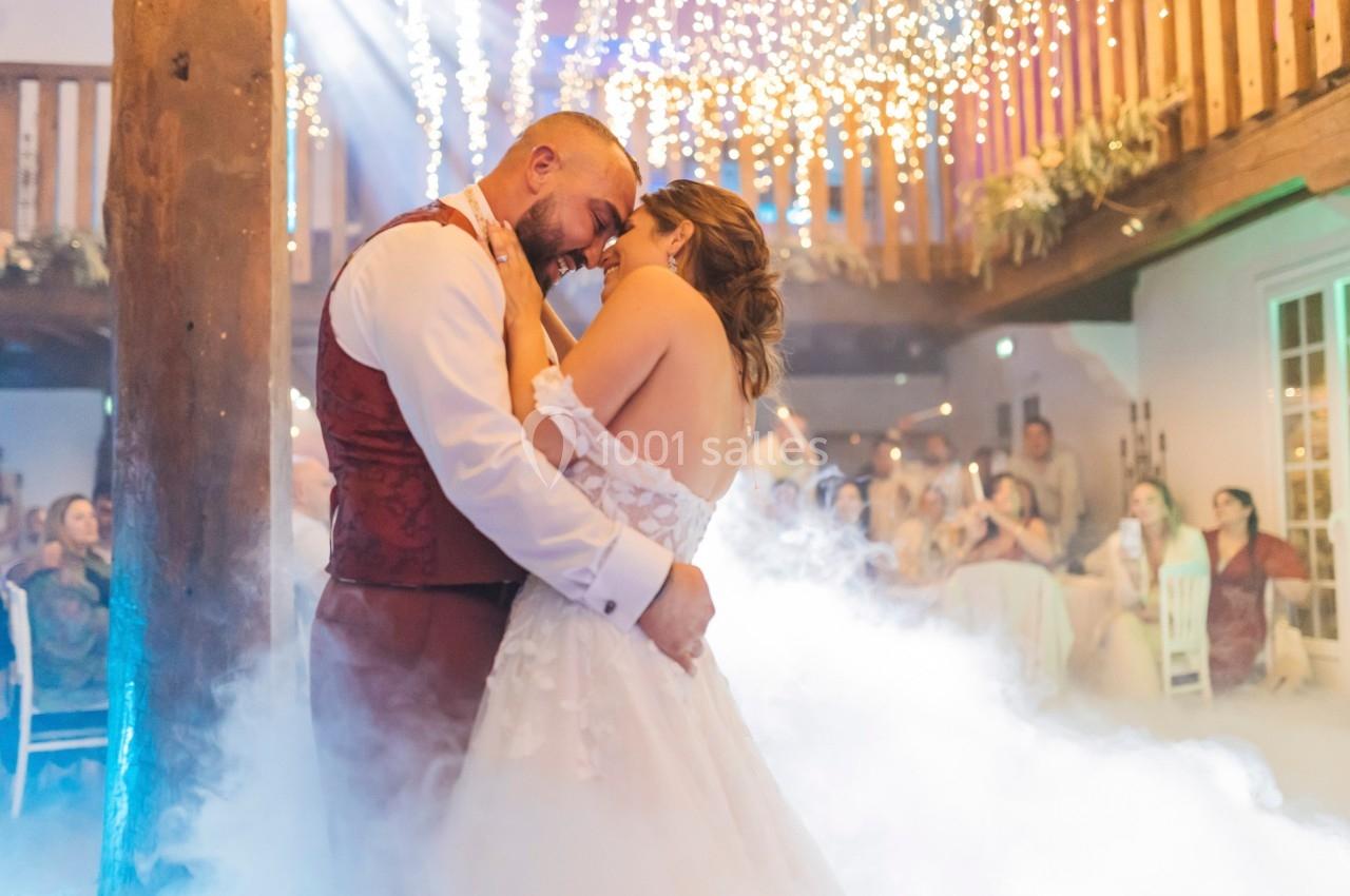 Un couple danse tendrement sous des lumières scintillantes dans une salle décorée, entouré de fumée légère.