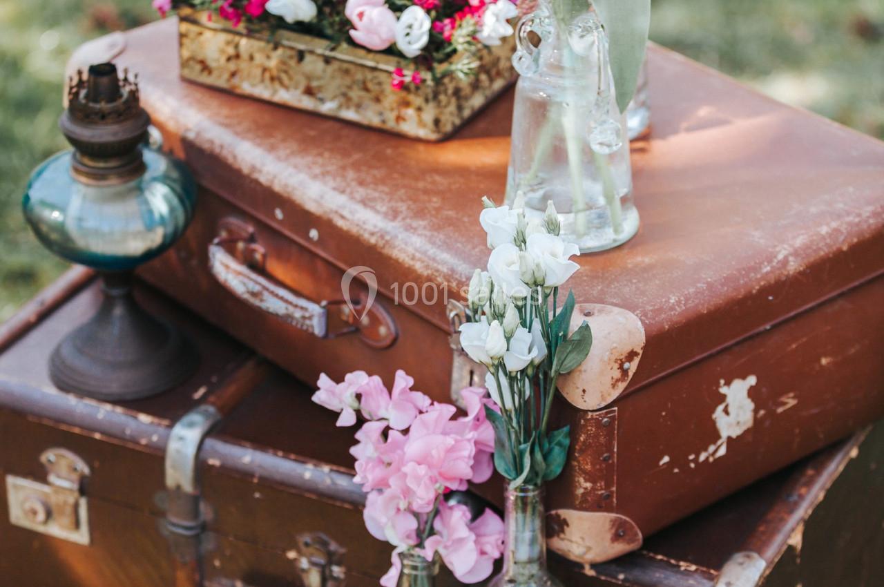 Des valises vintage empilées décorées de fleurs fraîches dans des vases en verre, disposées en extérieur.