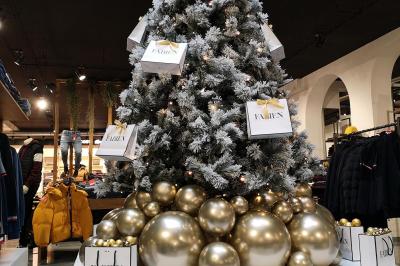 Sapin de Noël décoré de boules dorées et entouré de sacs cadeaux dans un magasin.