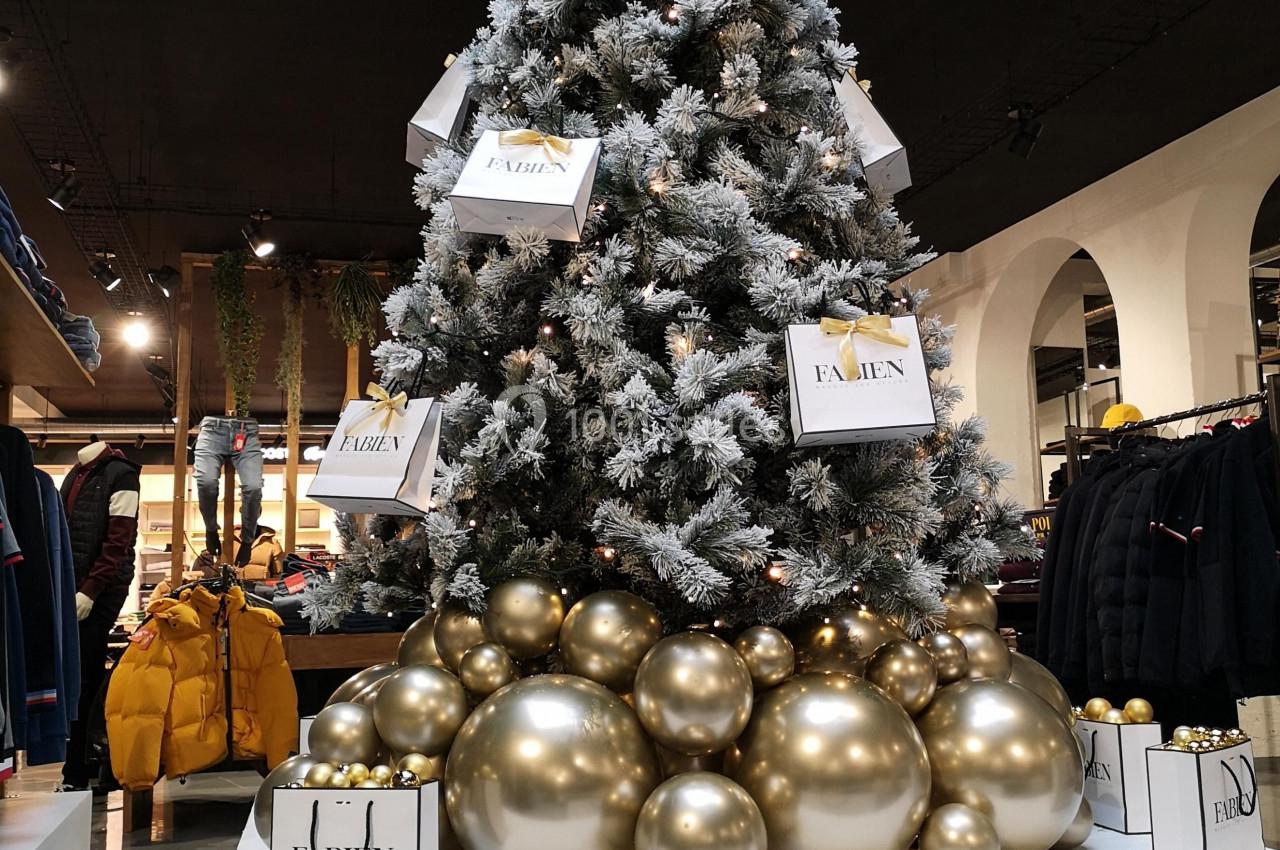 Sapin de Noël décoré de boules dorées et entouré de sacs cadeaux dans un magasin.