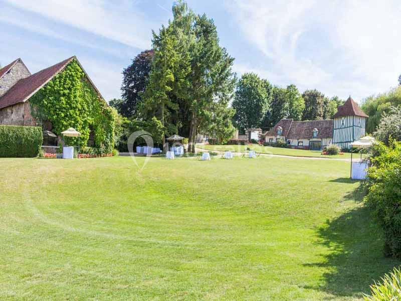 Grand jardin verdoyant avec pelouses bien entretenues, arbres, bâtiments traditionnels et parasols blancs disposés.
