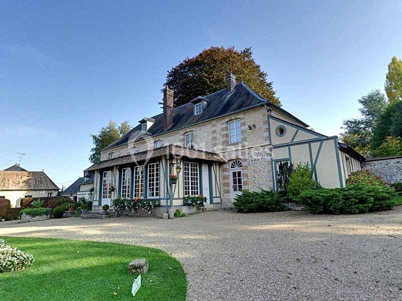 Façade d'une maison traditionnelle en pierre et colombages, entourée d'un jardin avec allée gravillonnée.