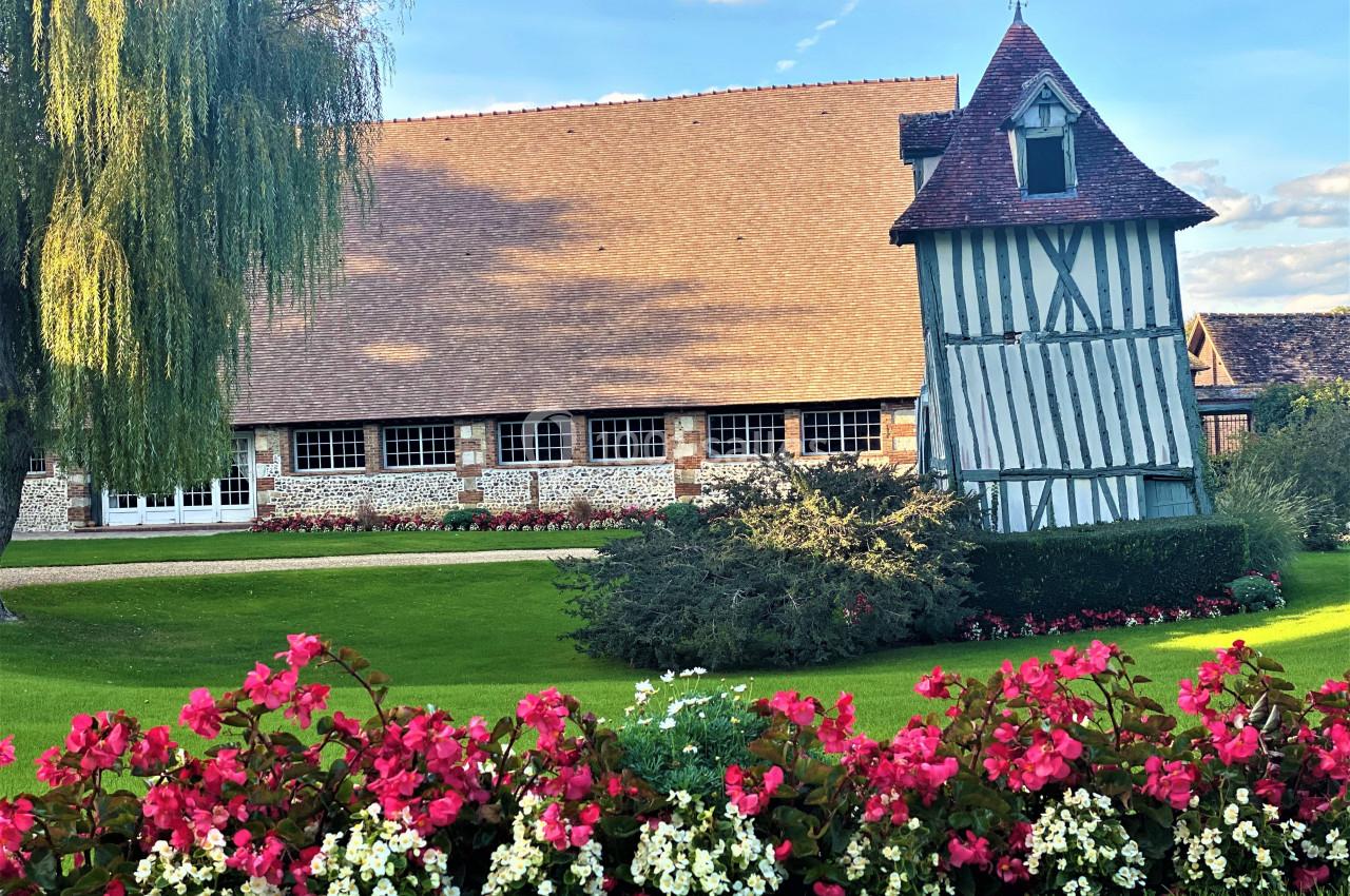 Bâtiment à colombages avec toit en tuiles, jardin fleuri au premier plan et ciel dégagé en arrière-plan.
