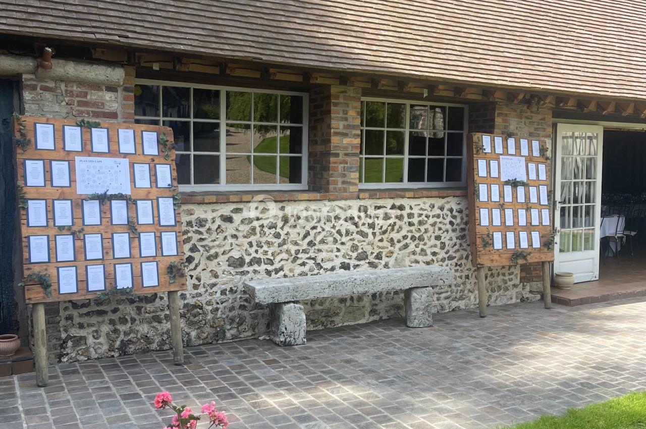 Façade en pierre avec deux panneaux d'affichage en bois, une jardinière fleurie et une porte vitrée sur la droite.