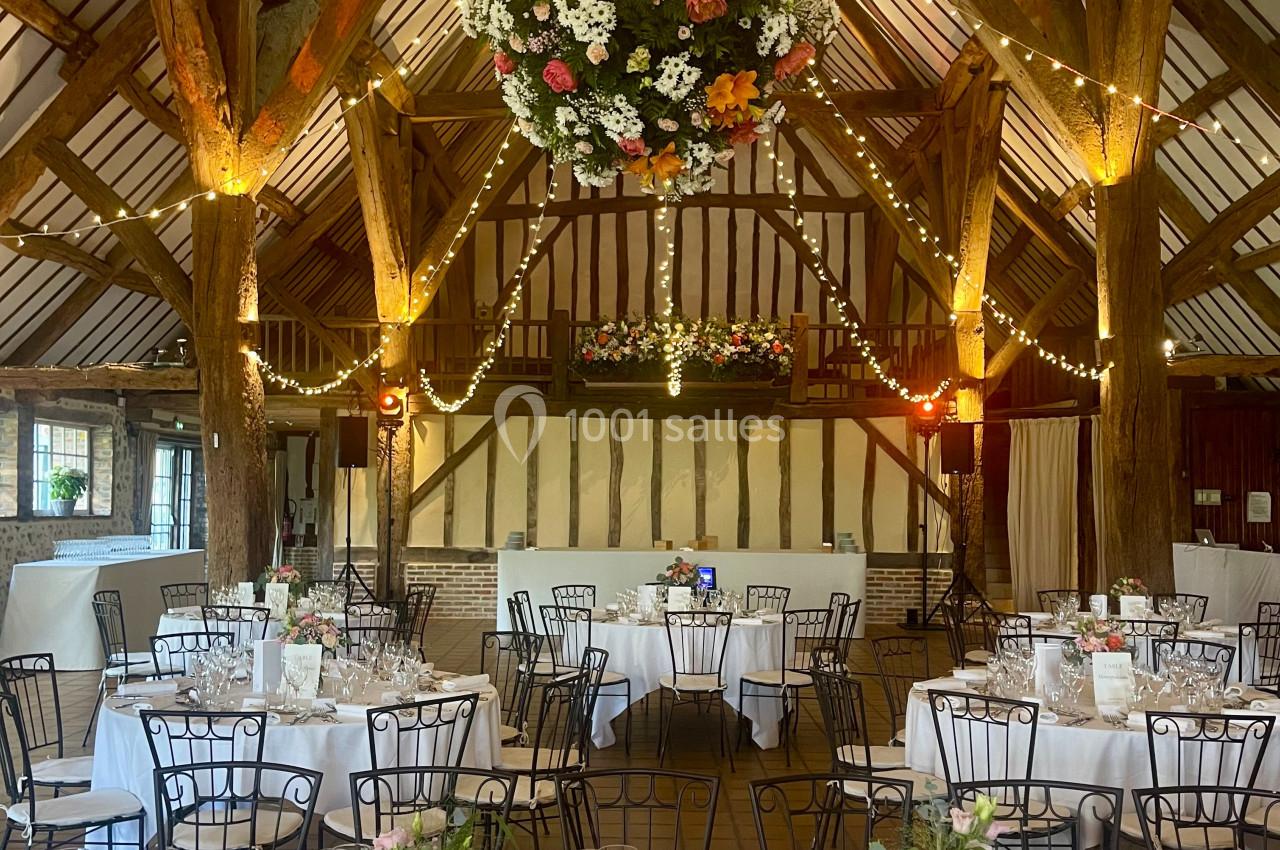 Salle de réception rustique décorée de guirlandes lumineuses, fleurs suspendues et tables dressées pour un événement.