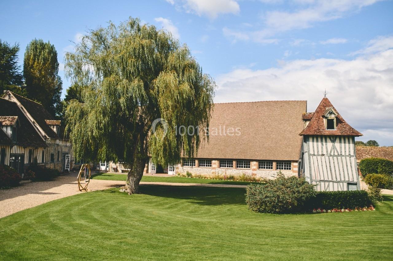 Bâtiments traditionnels à colombages entourés d'un jardin verdoyant avec un grand saule au premier plan.