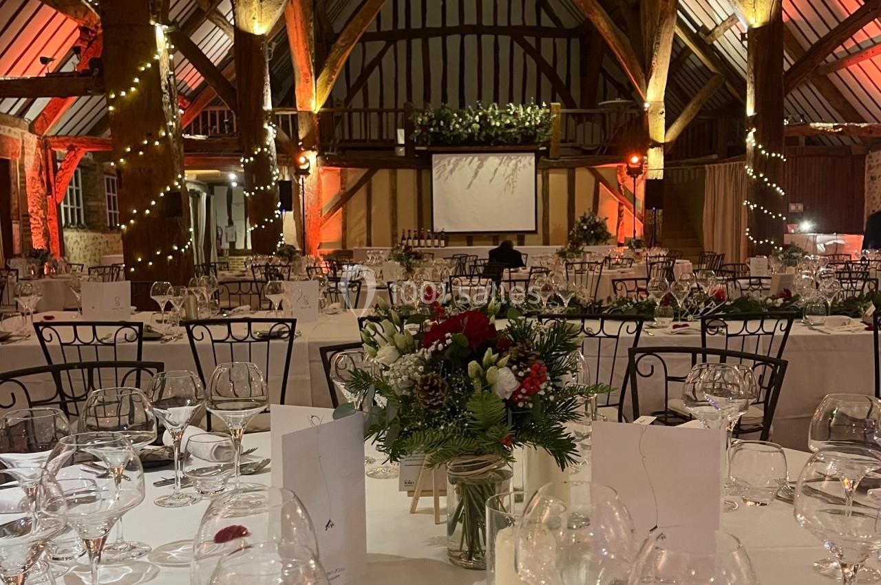 Grande salle de réception avec charpente apparente, tables dressées, décorations florales et éclairage chaleureux.