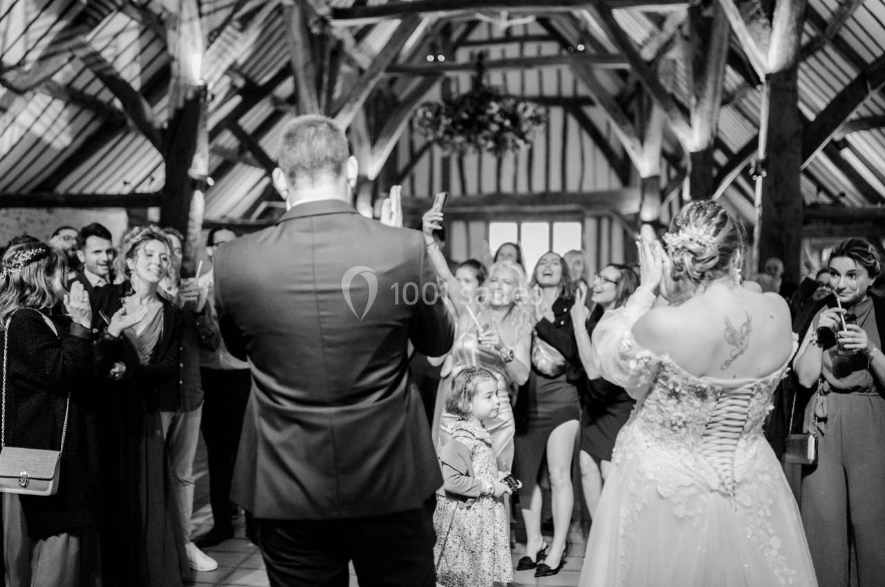 Un couple de mariés fait face à des invités applaudissant dans une salle avec une charpente en bois apparente.