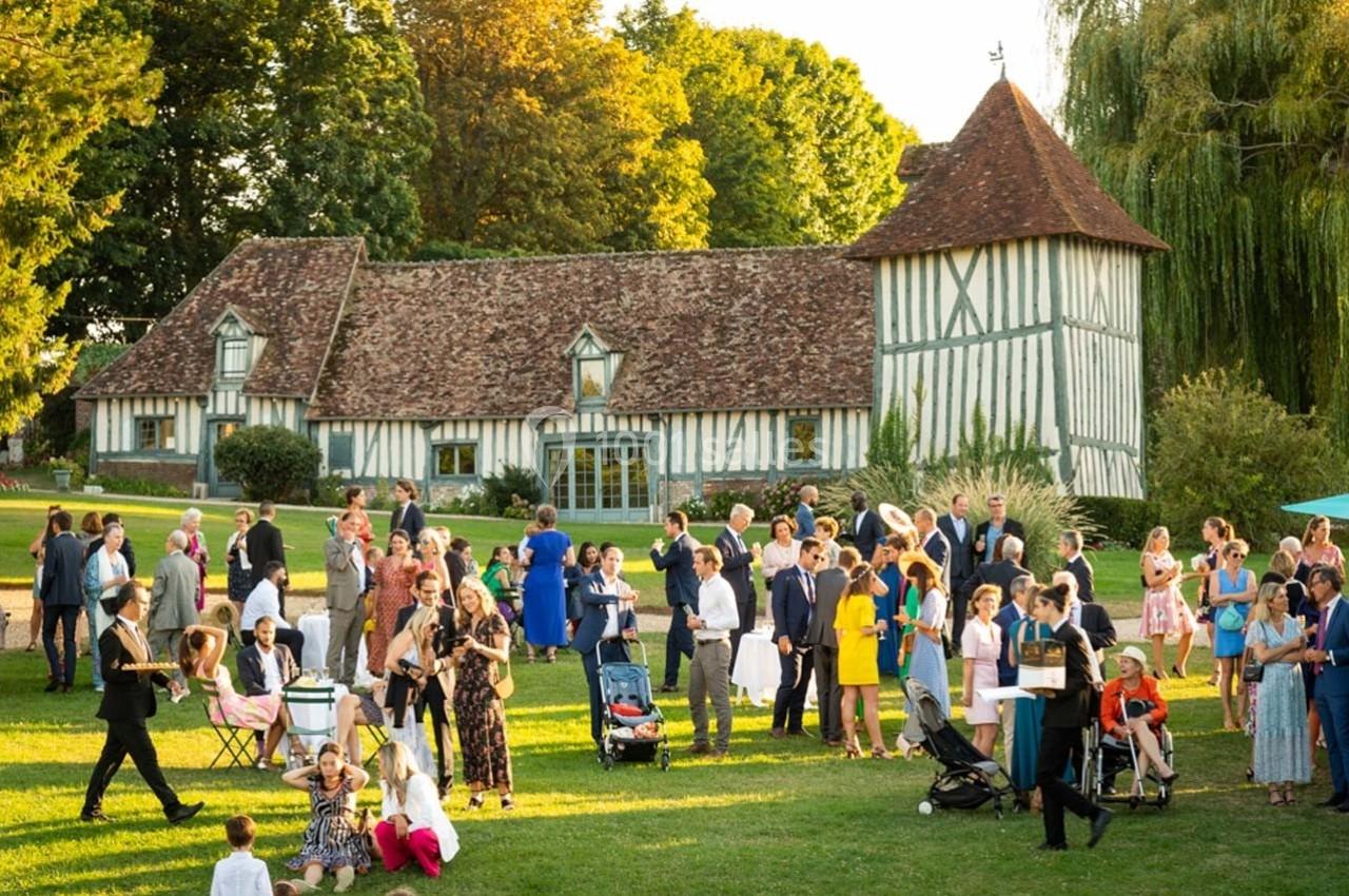 Groupe de personnes rassemblées dans un jardin devant une maison à colombages, lors d'un événement en plein air.