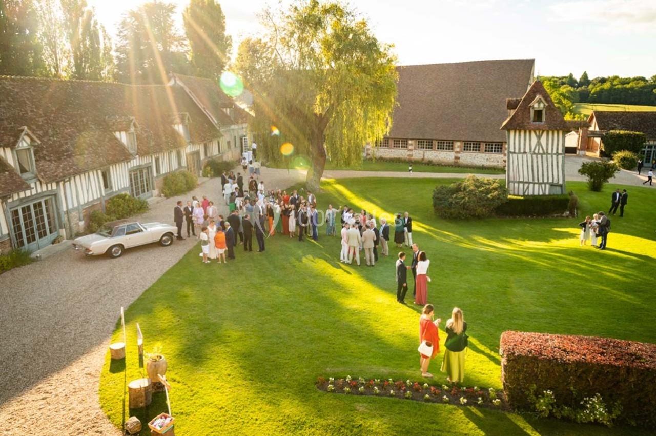 Groupe de personnes rassemblées dans un jardin verdoyant près de bâtiments à colombages sous une lumière ensoleillée.