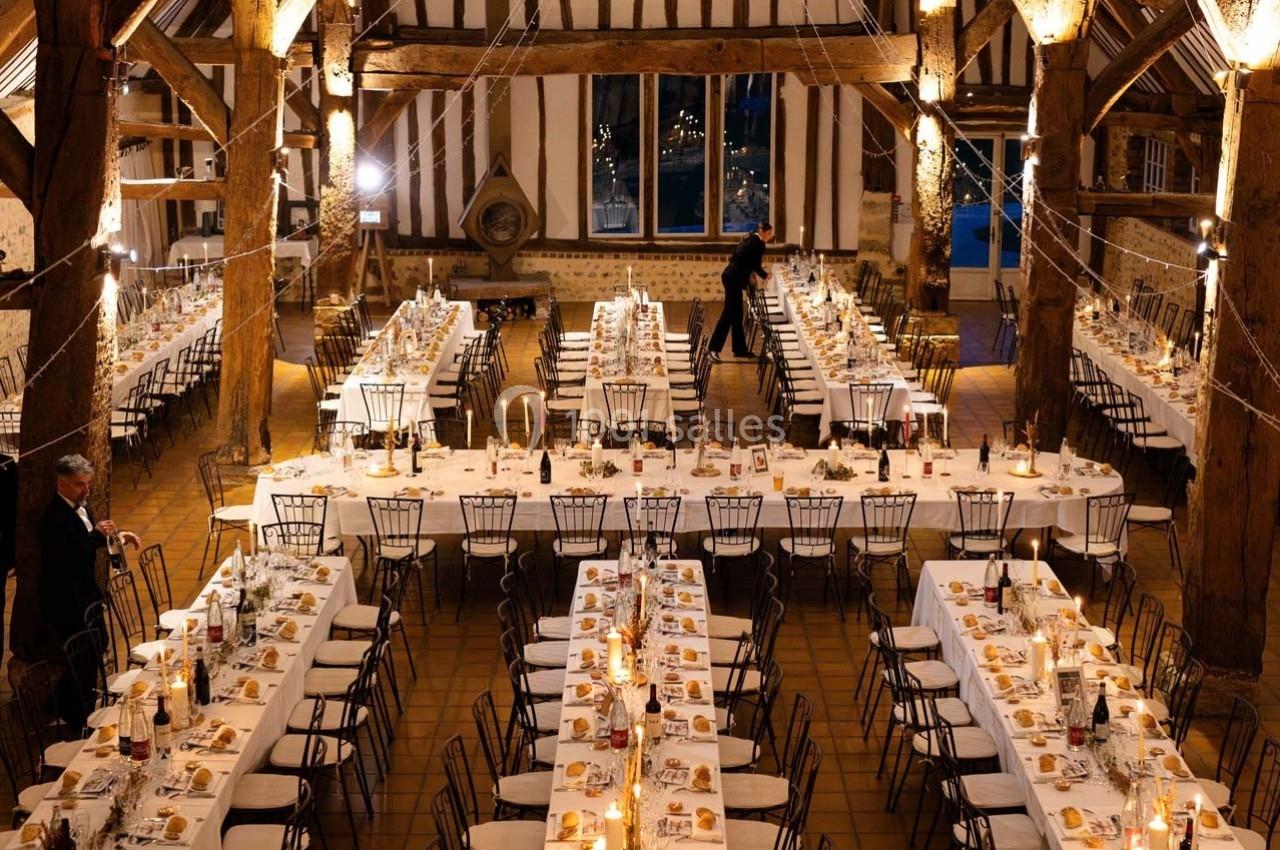 Grande salle de réception avec de longues tables dressées, décorée de lumières suspendues et d'éléments rustiques.
