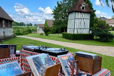 Platines vinyles et disques exposés sur une table en extérieur, avec un jardin verdoyant et un pigeonnier à colombages en…