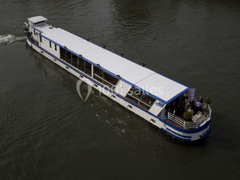 Bateau de croisière fluviale naviguant sur une rivière, avec des passagers à l'arrière.