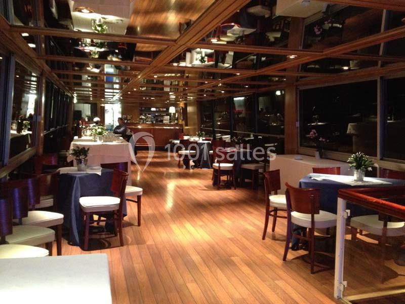 Salle de restaurant élégante avec parquet en bois, tables dressées et grandes fenêtres offrant une vue extérieure.