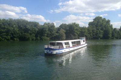 Salle de restaurant sur un bateau avec tables rondes dressées, nappes blanches et vue sur un paysage fluvial.