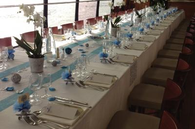 Salle de restaurant sur un bateau avec tables rondes dressées, nappes blanches et vue sur un paysage fluvial.