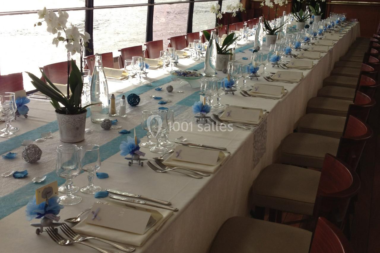 Table élégamment dressée avec nappes blanches, décorations bleues et blanches, et orchidées, dans une salle avec vue sur l…