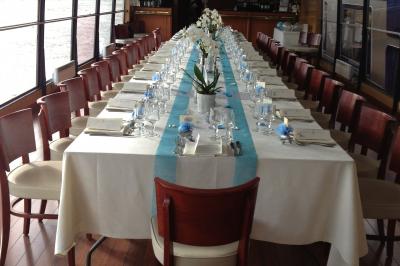 Salle de restaurant sur un bateau avec tables rondes dressées, nappes blanches et vue sur un paysage fluvial.