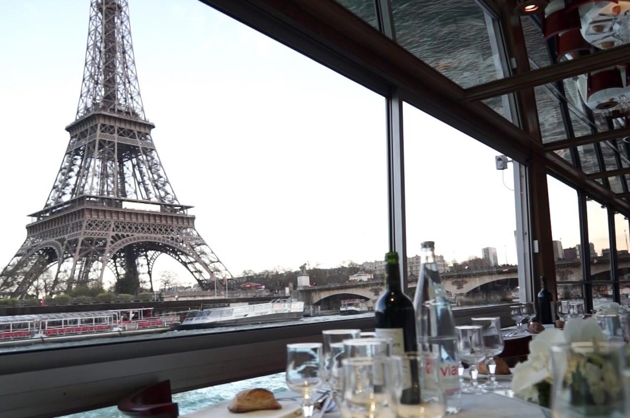 Vue de la Tour Eiffel depuis l'intérieur d'un restaurant avec une table dressée et des verres en premier plan.