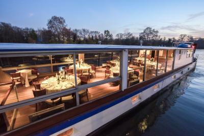 Salle de restaurant sur un bateau avec tables rondes dressées, nappes blanches et vue sur un paysage fluvial.