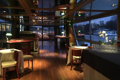 Salle de restaurant sur un bateau avec tables rondes dressées, nappes blanches et vue sur un paysage fluvial.