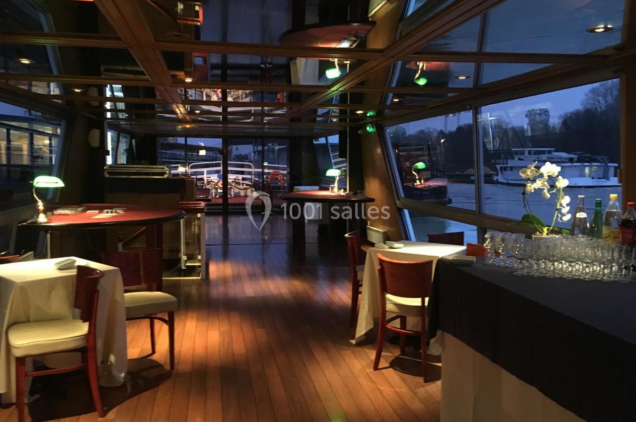 Salle de restaurant élégante avec parquet en bois, tables dressées et vue sur un quai au bord de l'eau.