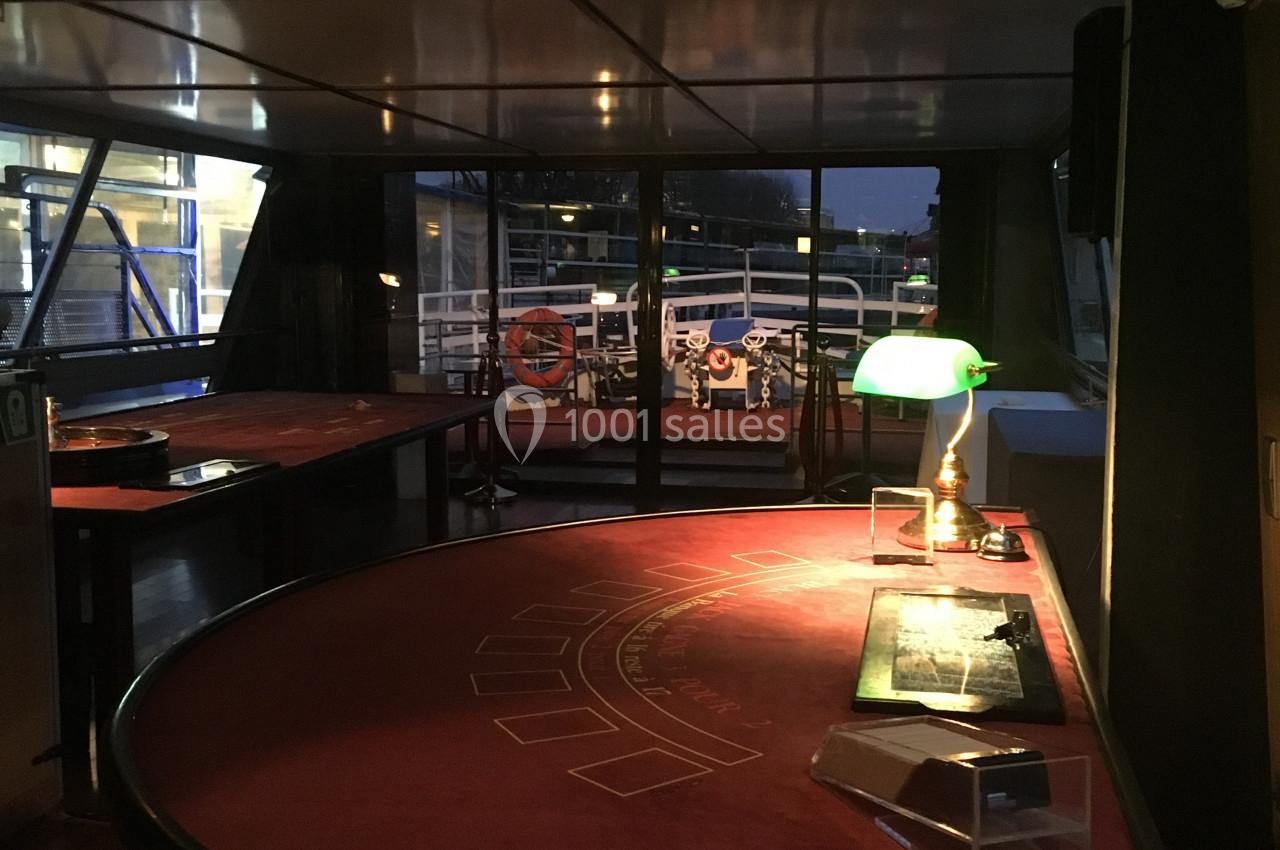 Salle avec une table de jeu rouge, une lampe verte allumée et une vue sur l'extérieur à travers des baies vitrées.