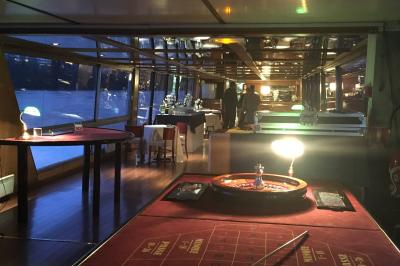 Salle de restaurant sur un bateau avec tables rondes dressées, nappes blanches et vue sur un paysage fluvial.