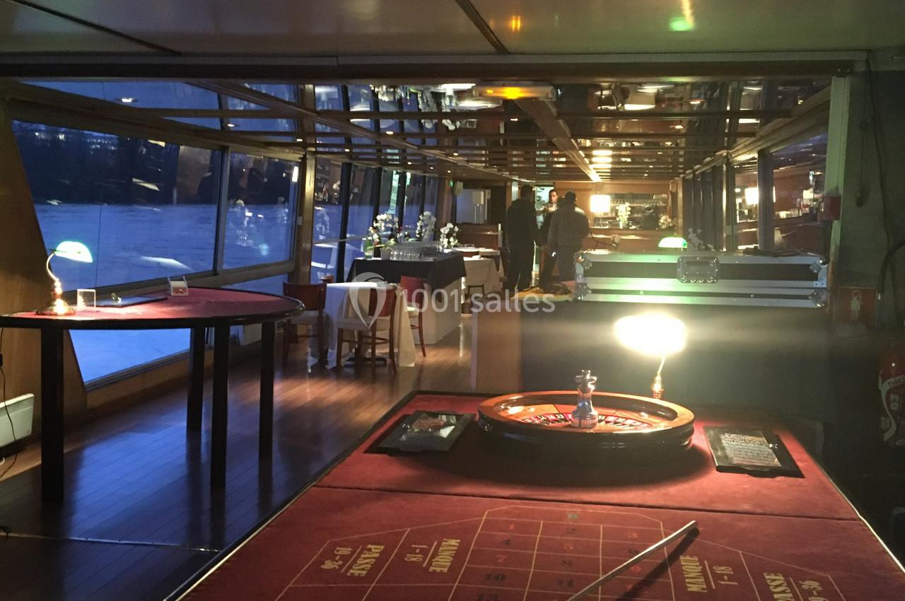 Salle de réception sur un bateau avec une table de roulette au premier plan et des tables dressées en arrière-plan.