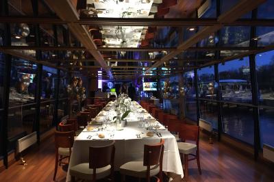 Salle de restaurant sur un bateau avec tables rondes dressées, nappes blanches et vue sur un paysage fluvial.