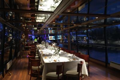 Salle de restaurant sur un bateau avec tables rondes dressées, nappes blanches et vue sur un paysage fluvial.