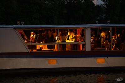 Salle de restaurant sur un bateau avec tables rondes dressées, nappes blanches et vue sur un paysage fluvial.