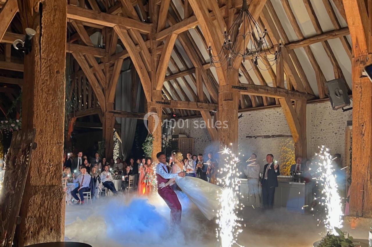 Un couple danse au centre d'une salle en bois avec des effets de fumée et des étincelles devant des invités.