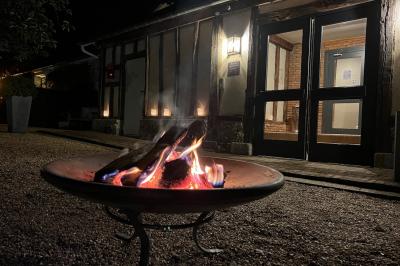 Miniature Location salle Corny (Eure) - Le Manoir de Corny #22 Brasero allumé dans une cour gravillonnée devant un bâtiment éclairé avec des murs en bois et des portes vitrées.