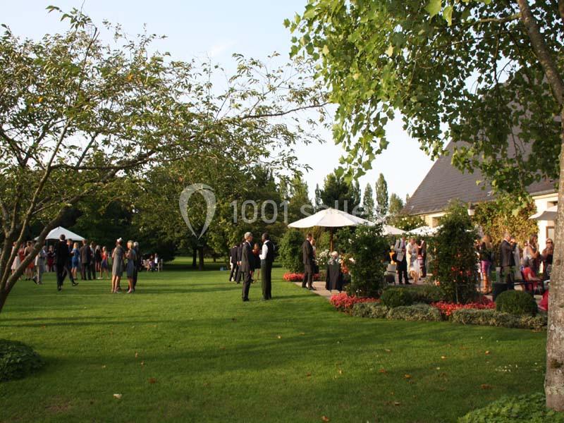 Personnes rassemblées dans un jardin verdoyant lors d'un événement en plein air, avec tentes et parasols.