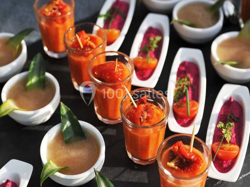 Assortiment de verrines et amuse-bouches colorés, comprenant soupes, sauces et légumes, disposés sur une table.