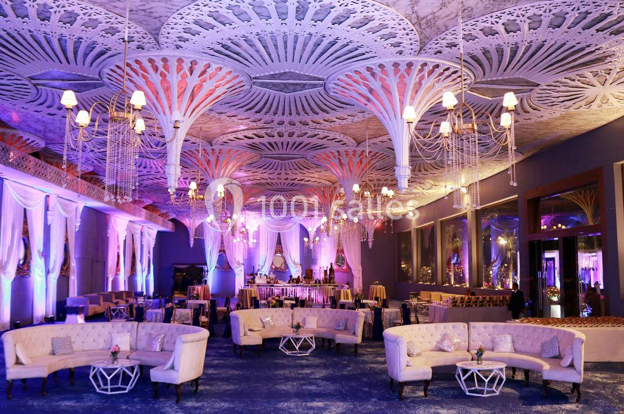 Salle de réception décorée avec des lustres, des plafonds ornés et des canapés disposés autour de tables basses.