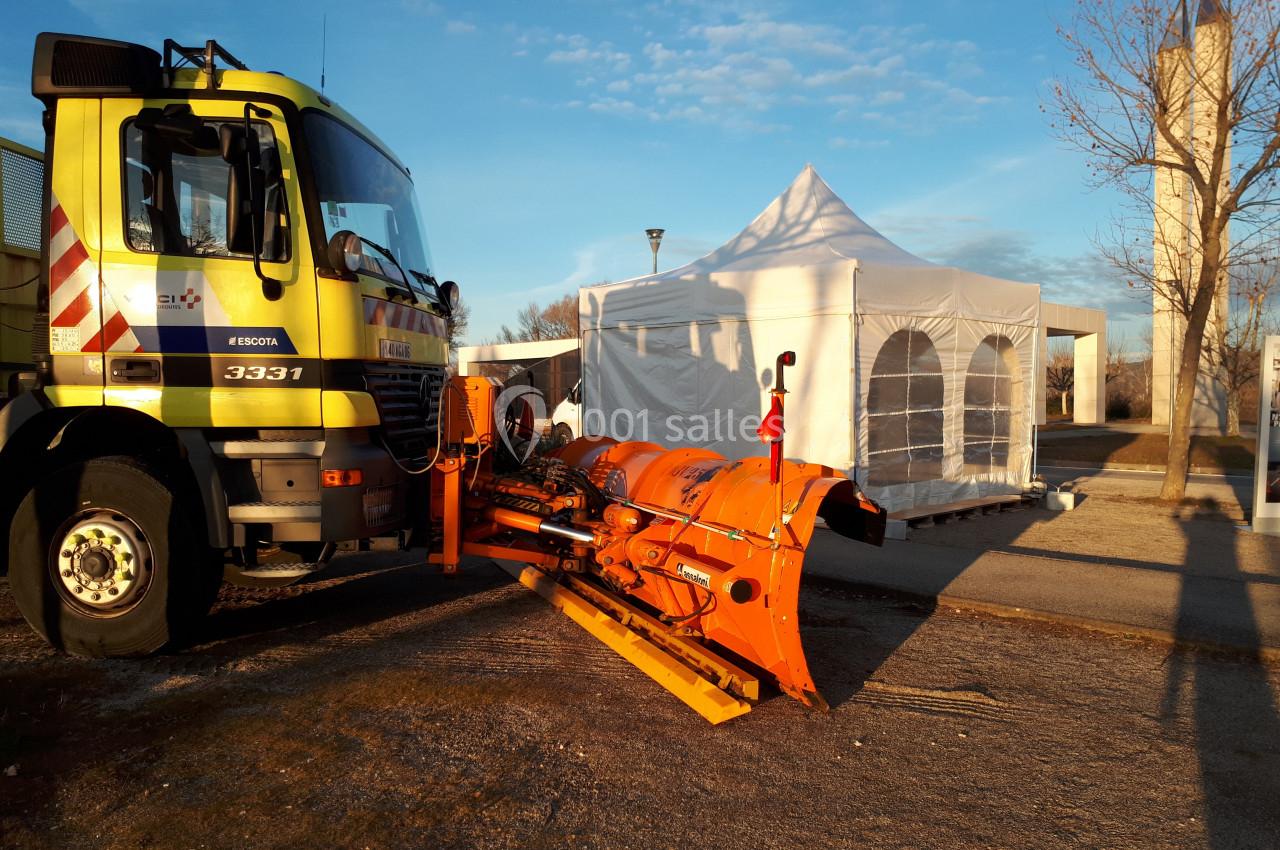 Camion équipé d'une lame de déneigement orange stationné près d'une tente blanche sur un terrain dégagé.