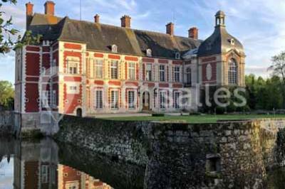 Bâtiment ancien avec façade décrépite, entouré d'une cour herbeuse et d'arbres dénudés en arrière-plan.