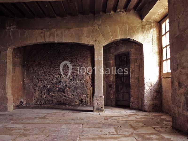 Intérieur d'une pièce ancienne avec murs en pierre, sol en dalles, poutres au plafond et une fenêtre laissant entrer la…