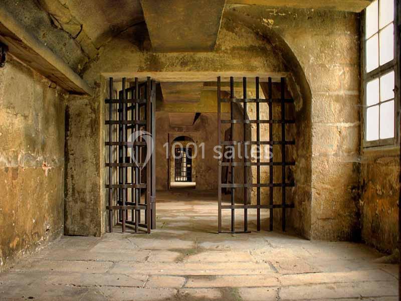 Vue intérieure d'une ancienne prison avec des murs en pierre, des grilles métalliques et des fenêtres laissant entrer la…